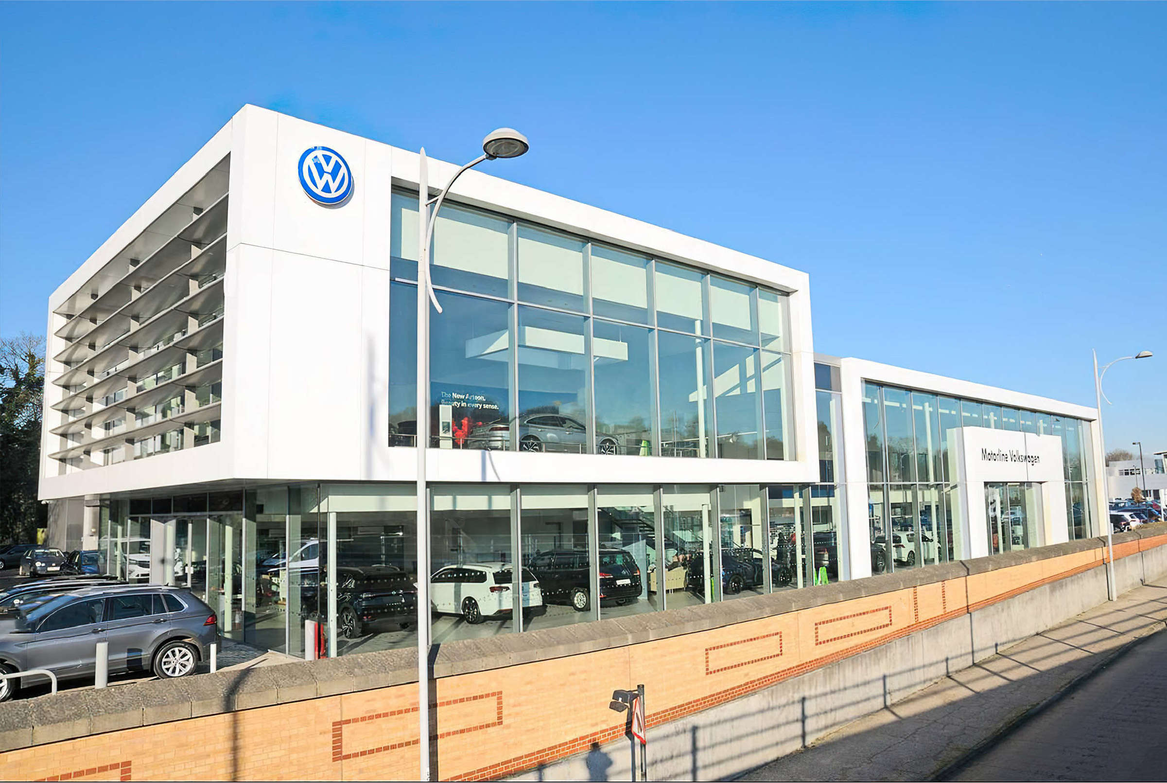 Two-storey car showroom with white composite panel cladding, full-height glazing and aluminium louvres
