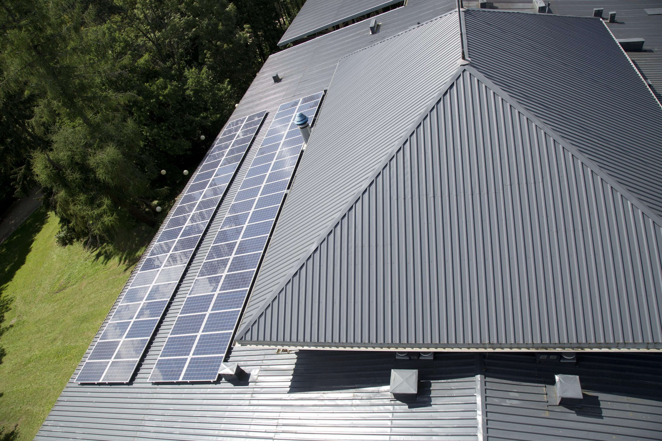 Grey profiled metal roof seen from above, with solar panels and roof vents across the sheets
