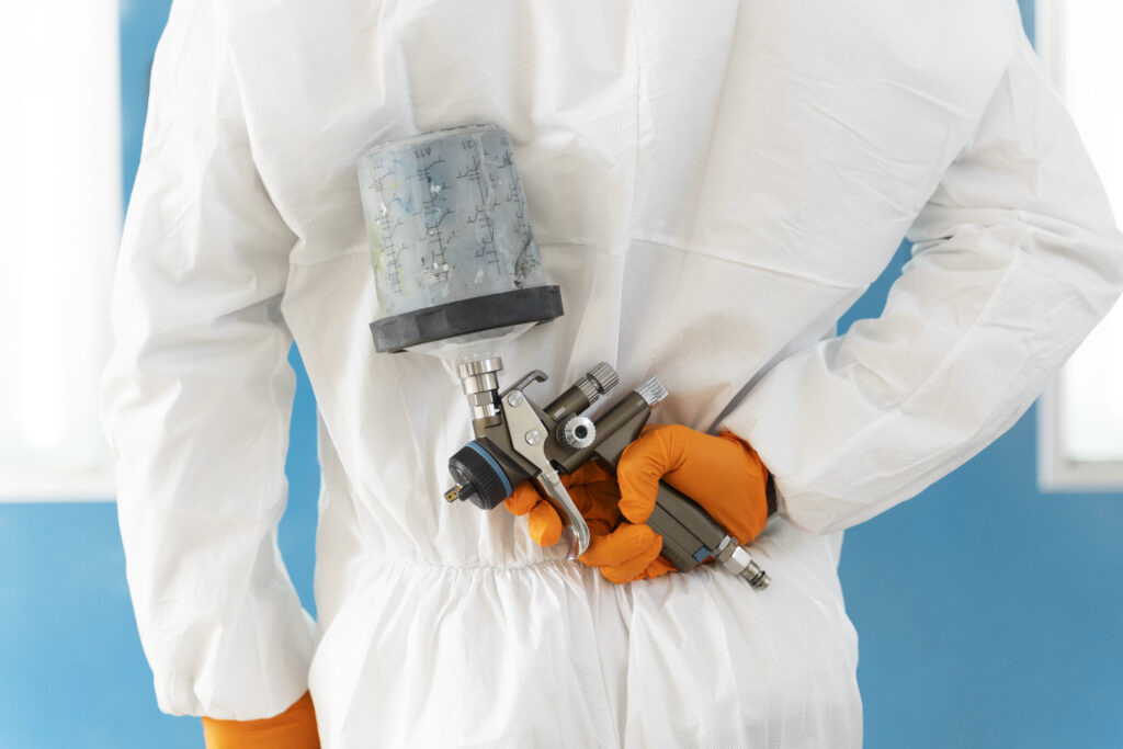 best-method-for-painting-cladding, the image shows a worker in white overalls holding an airless spray gun behind their back